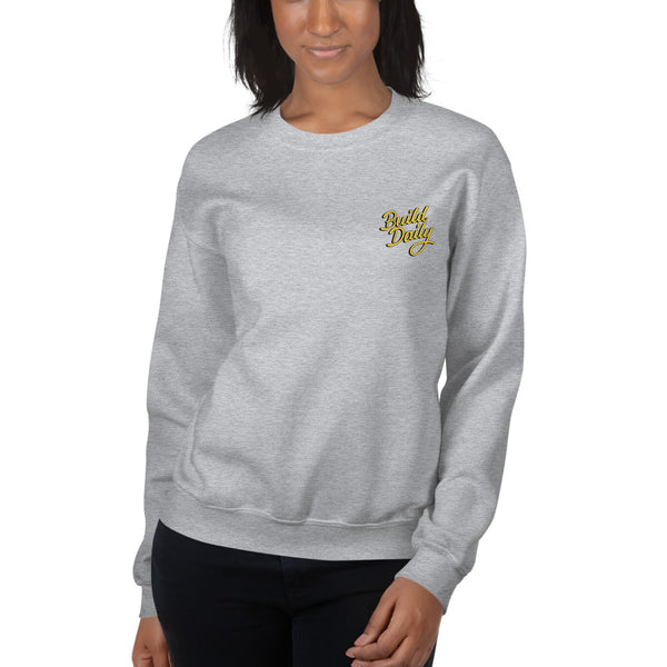 Woman wearing grey crewneck sweatshirt with yellow and black build daily signature logo